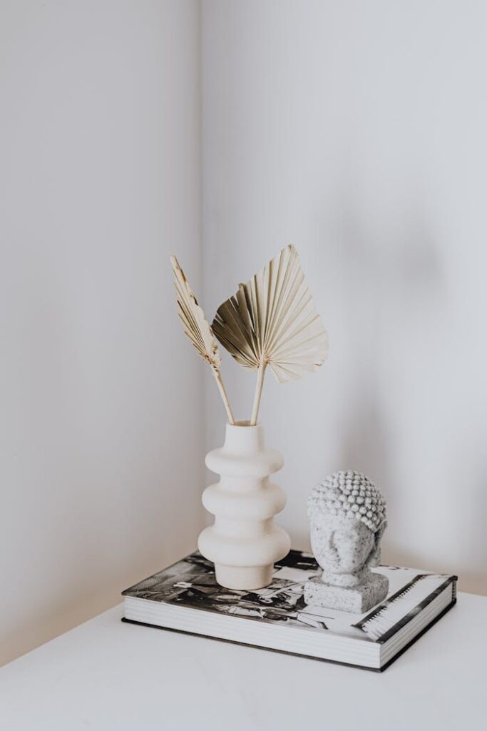 A serene interior decor setup featuring a ceramic vase with dried leaves and a Buddha statuette on a book.