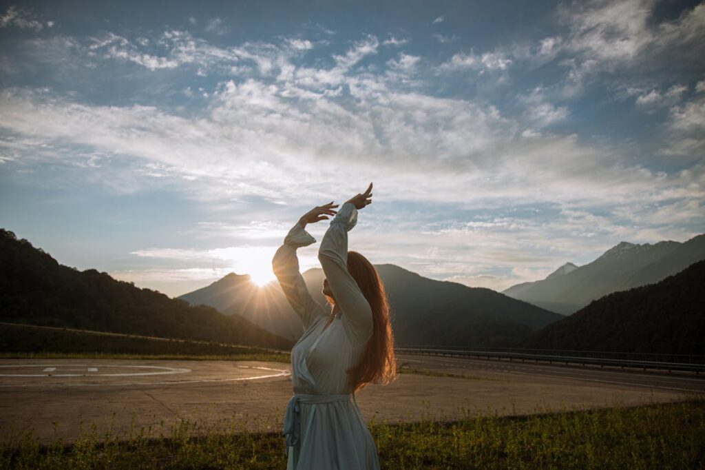 pexels photo 4937643 A woman gracefully dances with arms raised, set against a mountain sunset backdrop.